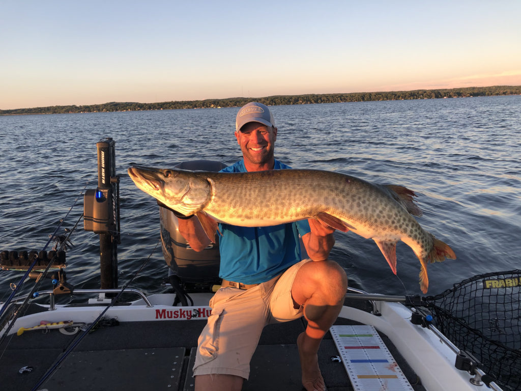 Man holding a huge muskie fish in boat on water