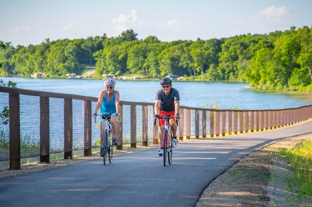 Couple riding bike by scenic lake as they follow the trails in Detroit Lakes