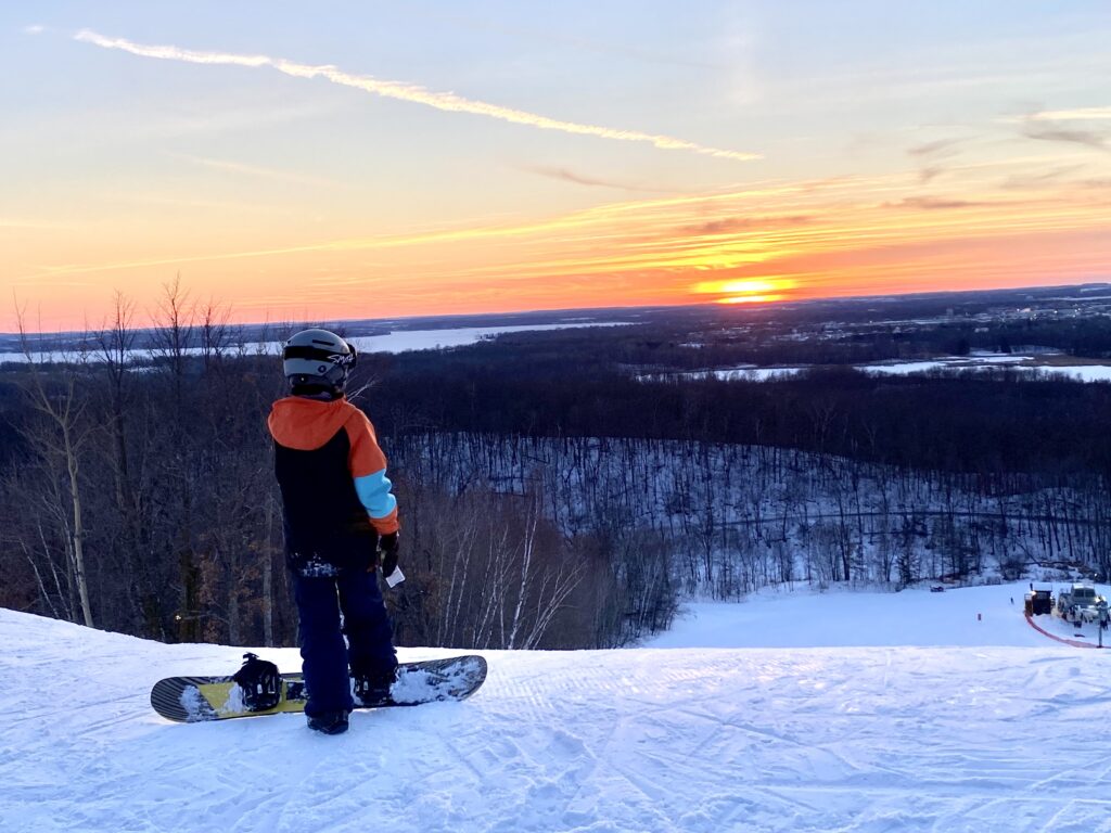 skier at top of mountain looking at sunset