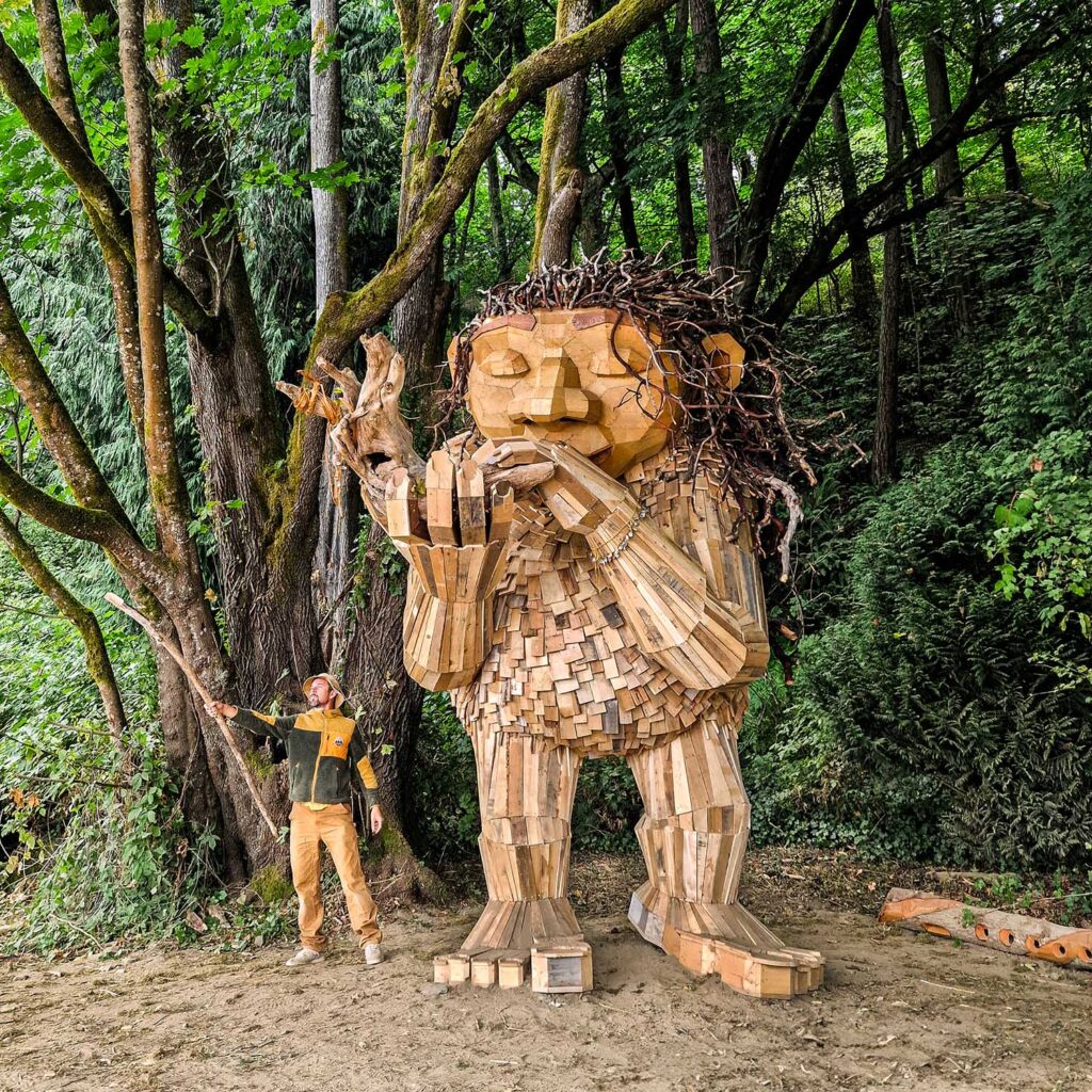 Thomas Dambo stands beside a huge wooden troll in the woods