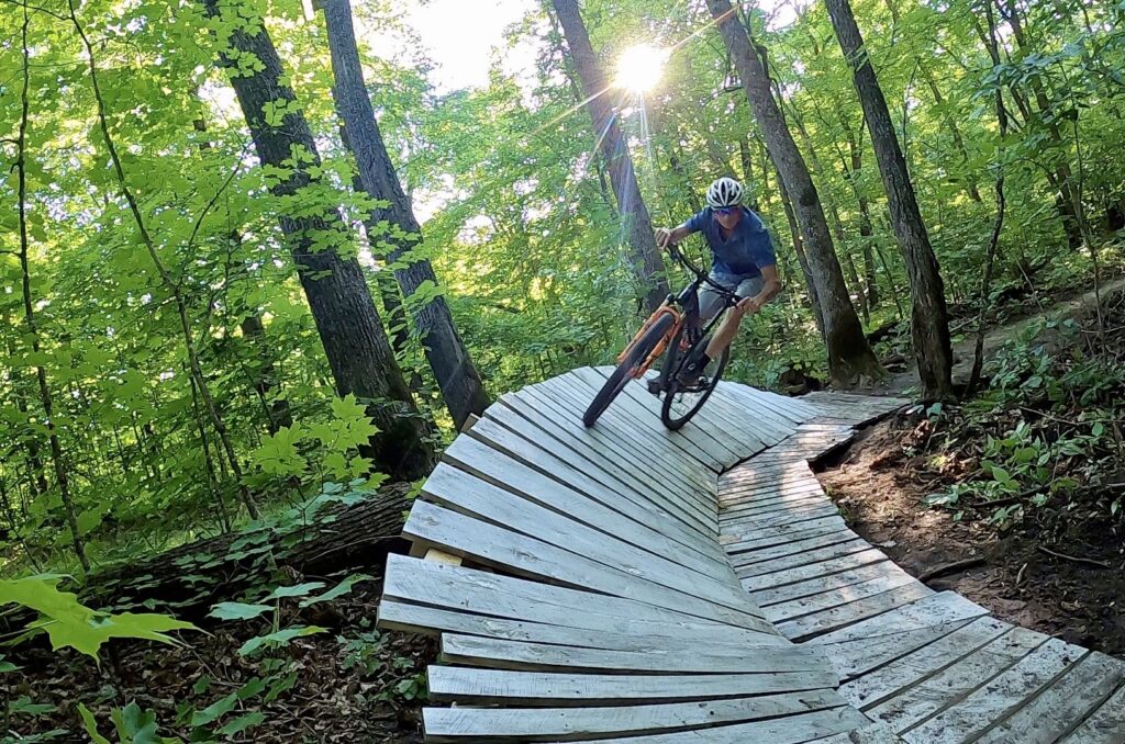 Guy mountain biking a wood ramp in a woods at Maplelag Resort