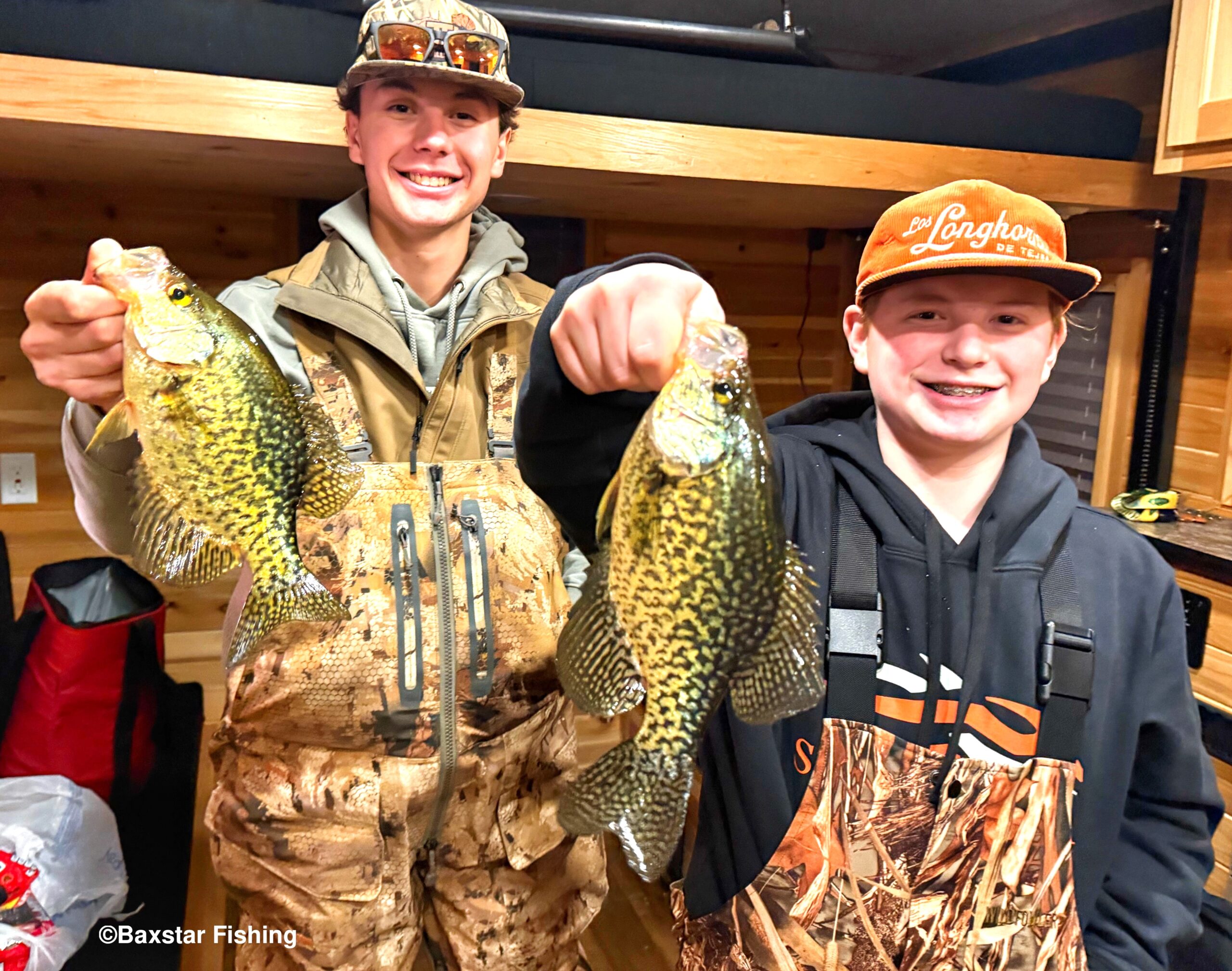two guys holding panfish they caught in ice fish house