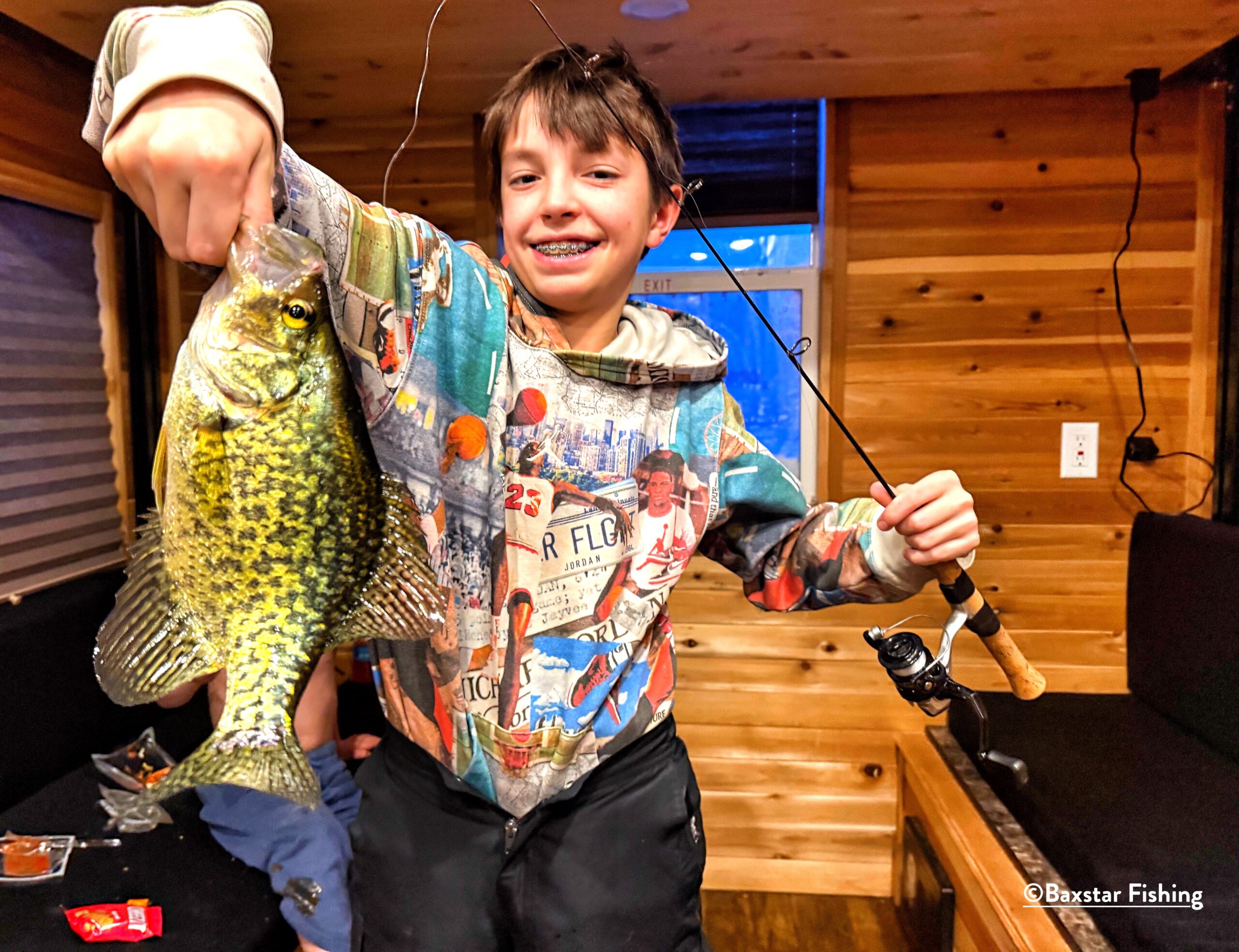 youth holding a nice crappie caught on a fishing pole in an ice fishing house