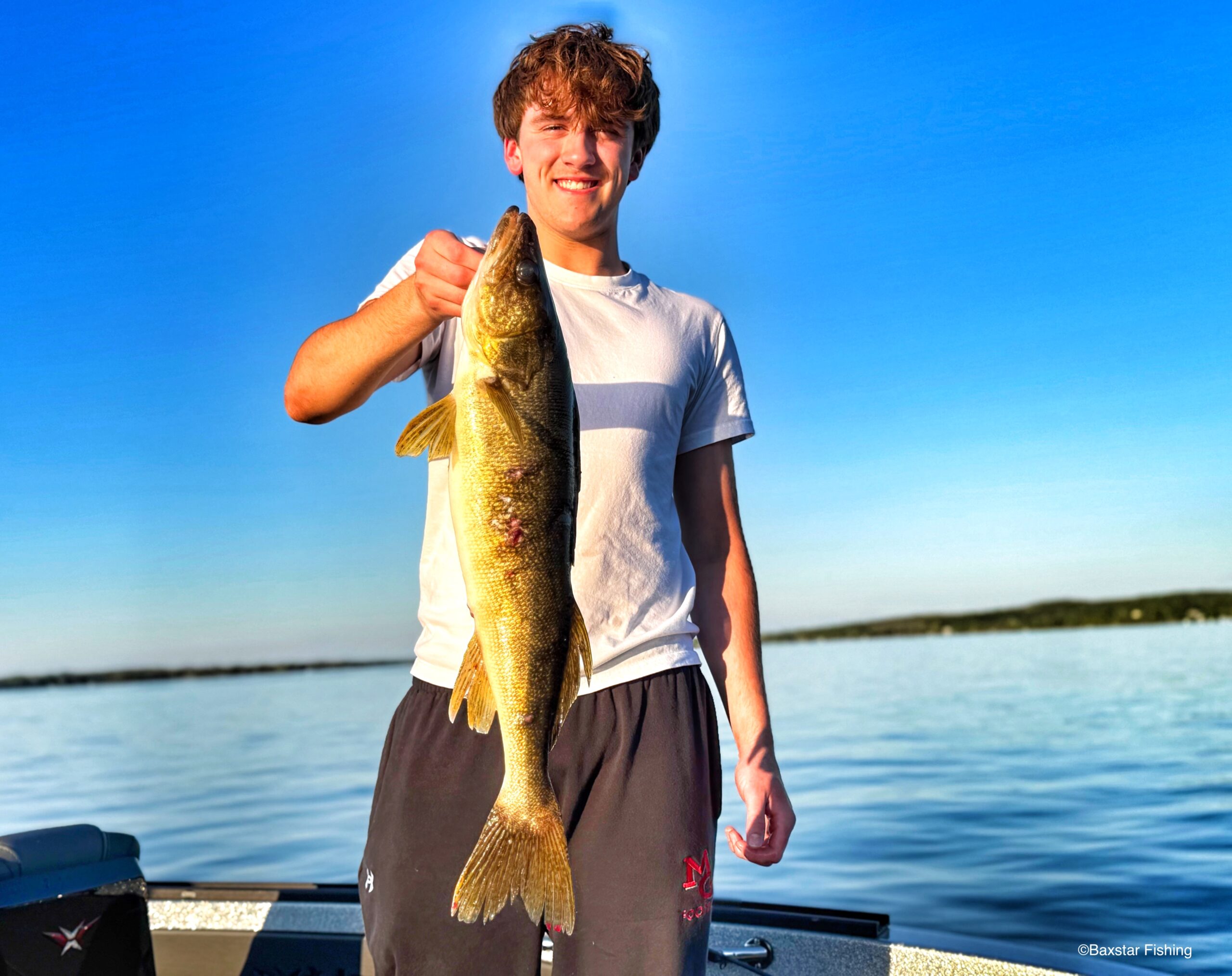 Young man holding a walleye while in a boat on the lake