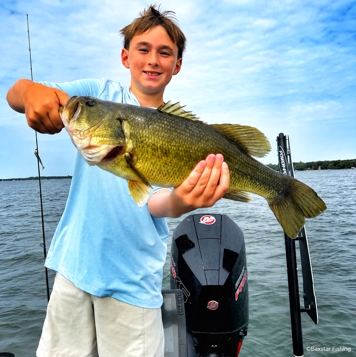 teenage boy holding large fish he caught in boat on lake